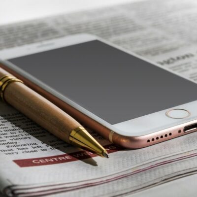 iPhone pictured next to a pen on top of a printed newspaper