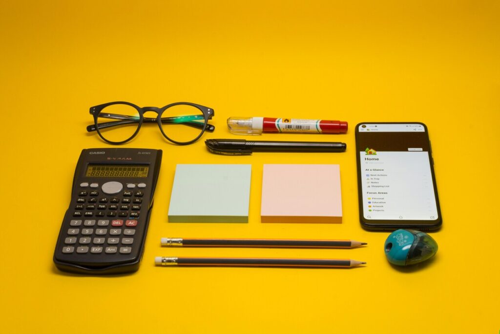 Calculator, mobile phone, post-it notes and pens laid out on a yellow background
