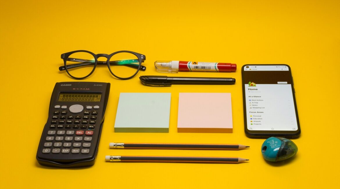 Calculator, mobile phone, post-it notes and pens laid out on a yellow background