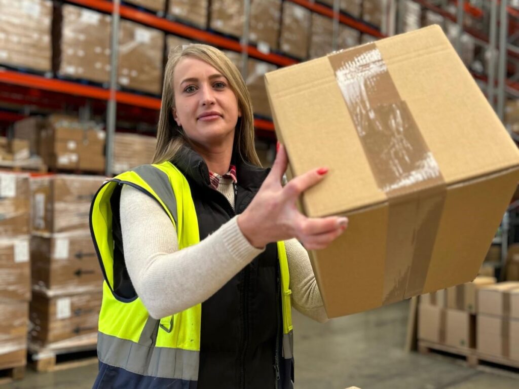 Supply chain professional wearing high vis holding up a brown box