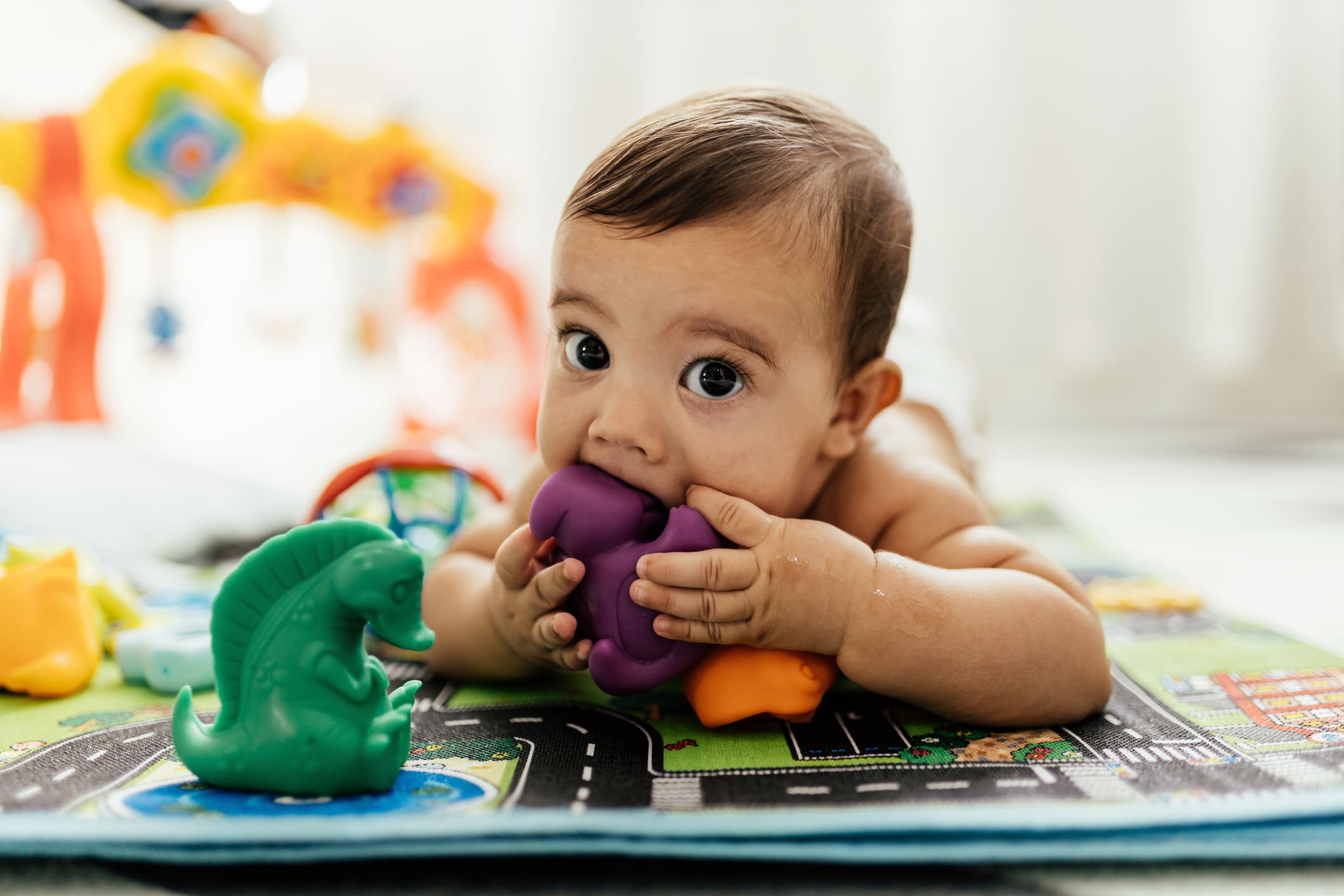 Baby pictured laying on its front chewing a toy