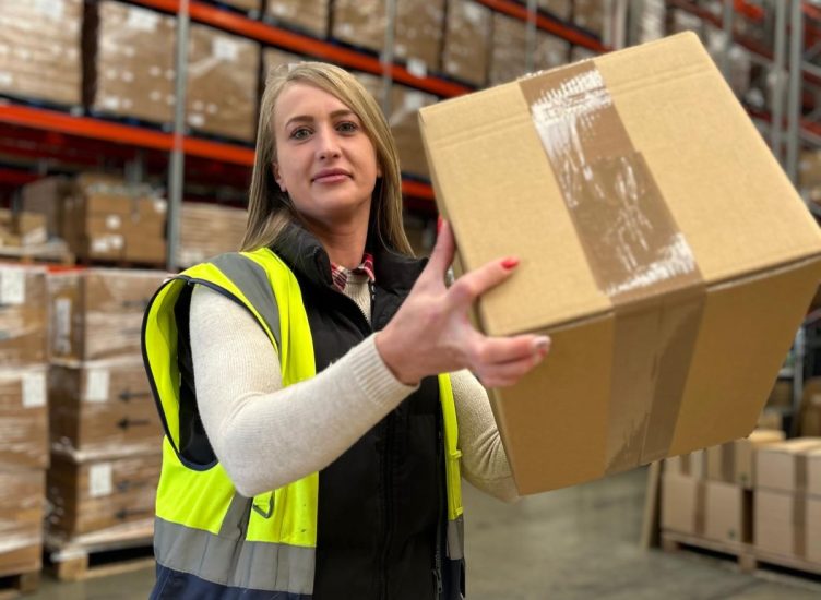 Supply chain professional wearing high vis holding up a brown box